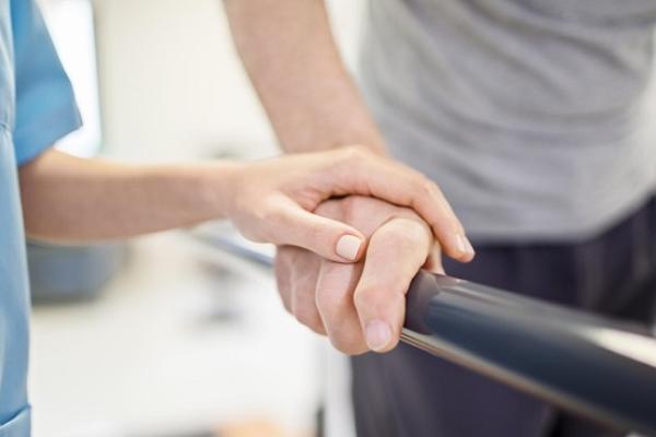 Carer's hand on a persons hand as they walk with a walking aid